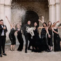 Un groupe joyeux célèbre un mariage noir et blanc, le marié ouvrant une bouteille de champagne sous une pluie de confettis.