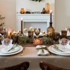 Une table de fête dressée avec une nappe intissé, des bougies, des verres ambrés et des décorations de Noël.