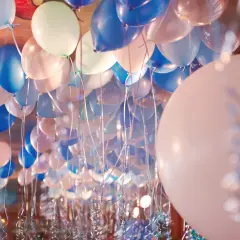 Une multitude de ballons bleus, blancs et roses flottent au plafond, prêts à être gonflés pour une fête.