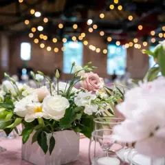 Un arrangement floral délicat, thème fleur, orne une table de réception rose. Des roses blanches et roses se mêlent à des fleurs plus petites et du feuillage vert.