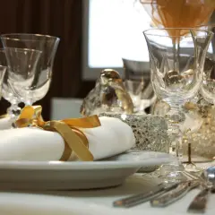 Service plat sur table avec des verres en cristal, des serviettes blanches nouées de ruban doré et des décorations scintillantes.