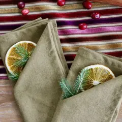 Un pliage serviette original avec une tranche d'orange séchée et une branche de sapin, sur une nappe rayée aux couleurs vives.