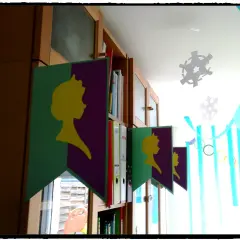 Guirlande "décoration reine des neiges à faire soi même" avec silhouettes jaunes sur fond violet et vert, suspendue devant une bibliothèque.