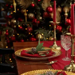 Une élégante deco table noel rouge et or, avec des bougies, des ornements dorés et un sapin scintillant en arrière-plan.