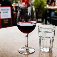 Un verre à vin rouge et un verre à eau sur une table de terrasse.