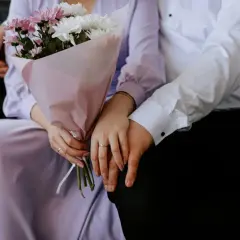 Un couple se tient la main, un bouquet de fleurs roses et blanches à la main. Un rappel doux de leur calendrier noces.