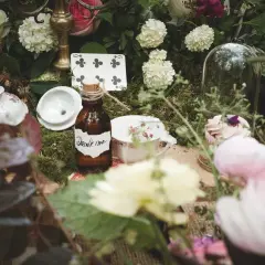 Décoration de mariage thème Alice au Pays des Merveilles : théière, cartes à jouer, et la fameuse bouteille "Drink me" sur un lit de mousse.