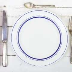 Une assiette blanche à double bordure bleue, une serviette à carreaux rouges et blancs, un couteau, une fourchette et deux cuillères. Qui a inventé les couverts ?