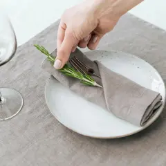Une main dépose une branche de romarin sur un pliage de serviette mariage boheme, sur une assiette blanche.