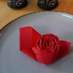 Un pliage serviette papier en forme de rose rouge sur une assiette grise. Une touche d'élégance pour une table.