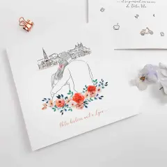 Un faire-part avec un dessin de couple devant une ville, orné de fleurs. Le texte "Notre histoire naît à Lyon..." suggère un événement spécial.