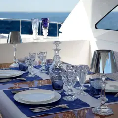 Un dîner élégant sur un yacht, avec des verres en cristal, des carafes et les différents couverts de table disposés sur des nappes bleues.