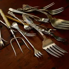 Un assortiment de fourchettes anciennes, certaines ornées, sur fond de bois. Qui a inventé la fourchette ? Ces ustensiles racontent une histoire.