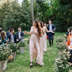 Le cortège d'église pour ce mariage en extérieur est joyeux. Les demoiselles d'honneur, en robes fluides, marchent sur l'herbe, applaudies par les invités.