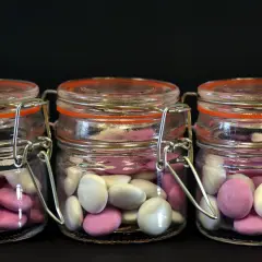 Trois bocaux en verre remplis de bonbons roses et blancs, une idée originale par quoi remplacer les dragées mariage.
