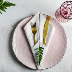 Service de table élégant avec pliage serviette communion, assiette rose, couverts dorés et verre à facettes.