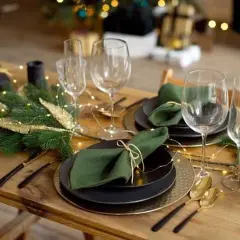 Table dressée pour Noël avec pliage serviette avec rond de serviette, guirlande lumineuse et branches de sapin.
