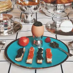 Un festin de caviar, toasts, œufs et fruits sur une table dressée avec une nappe au motif damassé.
