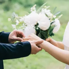 Un homme en costume met une bague à la main d'une femme, bouquet de fleurs blanches. Un poème mariage Baudelaire pour un amour éternel.