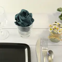 Un verre à pied, une serviette pliée en rose dans un verre, des petites fleurs et des couverts sur une table en bois.