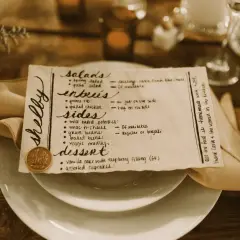 Un menu de mariage manuscrit, joliment présenté sur une assiette, détaille les entrées, accompagnements et desserts.