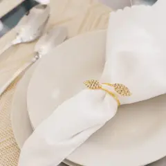Une serviette blanche mariage, ornée d'un anneau doré scintillant, repose sur une assiette. Des couverts argentés sont disposés à côté.