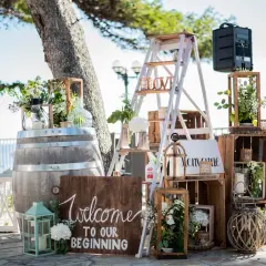 Décoration porte d'entrée pour mariage : un tonneau, une échelle décorée, des caisses en bois et des lanternes accueillent les invités.