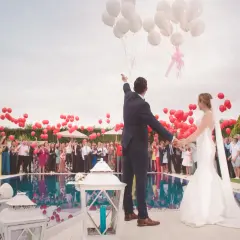 Un couple de mariés, entouré d'invités, lâche des ballons blancs et rouges. Un lâcher de ballon mariage symbolisant l'amour et l'espoir.