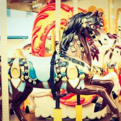 Chevaux décorés sur un manège de fête foraine, avec des touches de roses dans les ornements et les lumières.
