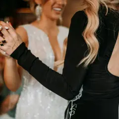 Deux femmes dansent, l'une en robe blanche scintillante, l'autre en robe noire. Elles se tiennent la main, un geste pour faire honneur au mariage.