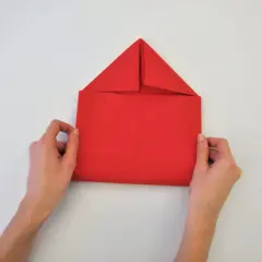 Mains tenant une feuille rouge pour un pliage serviette enveloppe. Le papier est plié en forme de maison.