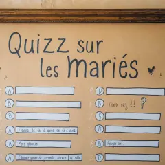 Un jeu mariage questions invités pour tester les connaissances sur les mariés. Le quiz est écrit à la main sur un fond brun.