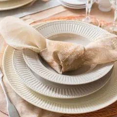 Une table dressée avec des assiettes empilées, une serviette en tissu nouée, une fourchette et des verres. La différence entre faïence et porcelaine est subtile, mais la qualité est évidente.