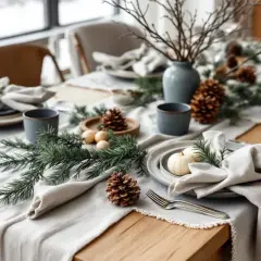 Une table dressée dans un esprit deco table nature chic, avec des pommes de pin, des branches de sapin et de petites citrouilles blanches.
