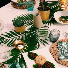 Une table dressée dans une ambiance jungle, avec des feuilles de palmier, des plantes en boîtes et des bougies.