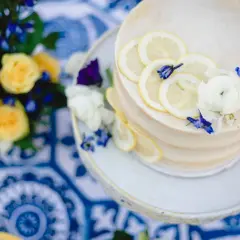 Gâteau de mariage jaune et bleu, décoré de rondelles de citron et de fleurs. Un bouquet de roses jaunes et de fleurs bleues est à proximité.