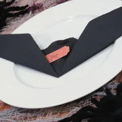 Une serviette noire pliée en forme de chauve-souris sur une assiette blanche, avec une étiquette "Joy". Décoration d'Halloween.