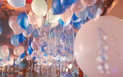 Une multitude de ballons bleus, blancs et roses flottent au plafond, prêts à être gonflés pour une fête.
