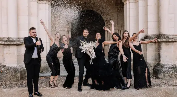 Un groupe joyeux célèbre un mariage noir et blanc, le marié ouvrant une bouteille de champagne sous une pluie de confettis.