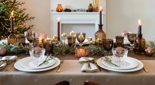 Une table de fête dressée avec une nappe intissé, des bougies, des verres ambrés et des décorations de Noël.
