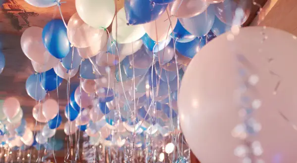Une multitude de ballons bleus, blancs et roses flottent au plafond, prêts à être gonflés pour une fête.
