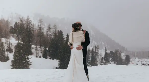 Un couple s'embrasse dans un paysage enneigé, un mariage thème montagne inoubliable.