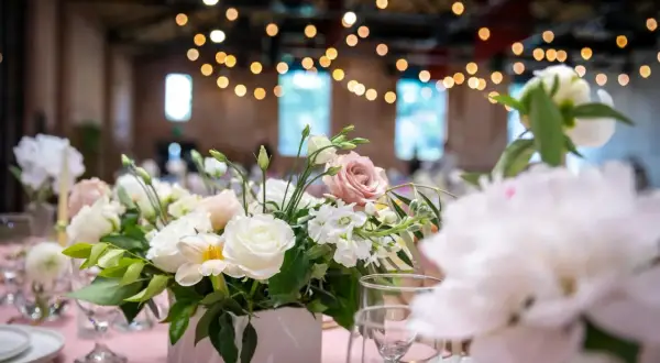 Un arrangement floral délicat, thème fleur, orne une table de réception rose. Des roses blanches et roses se mêlent à des fleurs plus petites et du feuillage vert.