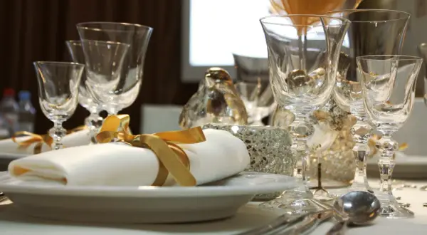 Service plat sur table avec des verres en cristal, des serviettes blanches nouées de ruban doré et des décorations scintillantes.