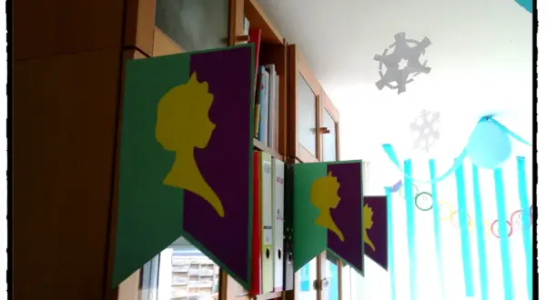 Guirlande "décoration reine des neiges à faire soi même" avec silhouettes jaunes sur fond violet et vert, suspendue devant une bibliothèque.