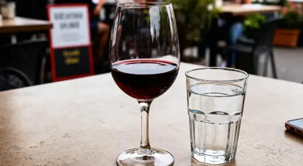 Un verre à vin rouge et un verre à eau sur une table de terrasse.