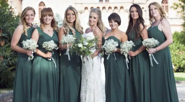 La mariée et ses demoiselles d'honneur, toutes en robes vert d'eau, tiennent des bouquets de fleurs blanches. Un mariage champêtre devant un château.