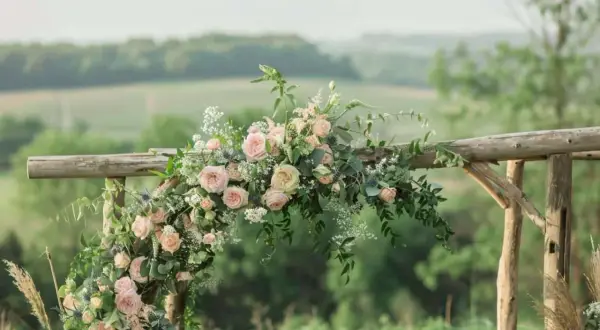 Un arc en bois rustique orné de roses roses et de verdure, parfait pour une cérémonie laïque champêtre.
