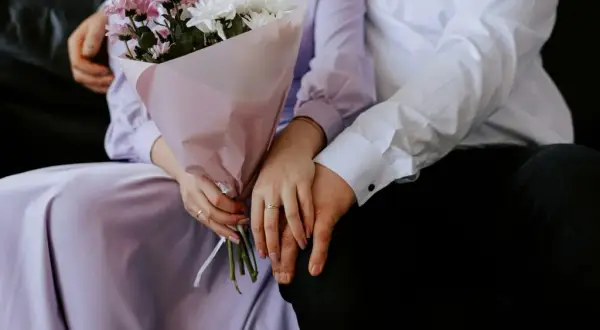 Un couple se tient la main, un bouquet de fleurs roses et blanches à la main. Un rappel doux de leur calendrier noces.