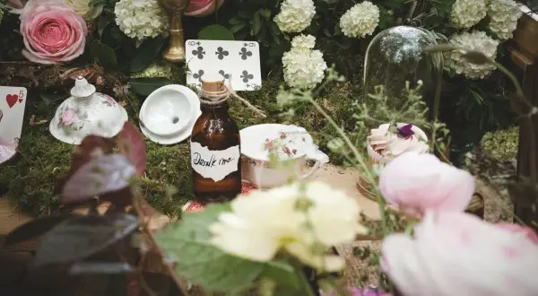 Décoration de mariage thème Alice au Pays des Merveilles : théière, cartes à jouer, et la fameuse bouteille "Drink me" sur un lit de mousse.